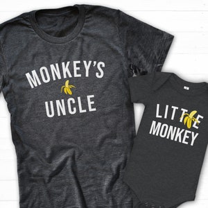 May include: Two dark gray t-shirts with white text and a banana graphic. The larger shirt says "Monkey's Uncle" and the smaller shirt says "Little Monkey".