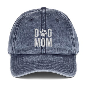 May include: A blue denim baseball cap with the text "DOG MOM" embroidered in white with a paw print in place of the "O".