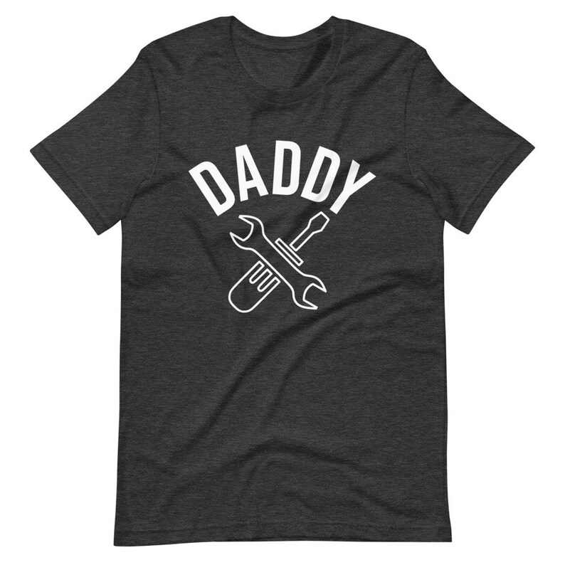 K&ouml;nnte beinhalten: Dunkelgraues T-Shirt mit einem wei&szlig;en Grafikdruck eines Schraubenschl&uuml;ssels und Schraubendrehers, die sich kreuzen, mit dem Wort "DADDY" dar&uuml;ber.