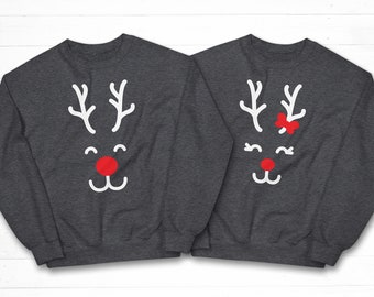 May include: Two gray sweatshirts with a white reindeer face design. One reindeer has a red bow on its antlers. The sweatshirts are a matching set.