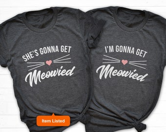 May include: Two gray t-shirts with white text that says "She's gonna get meowed" and "I'm gonna get meowed". The shirts have a pink heart and white whiskers above the text.