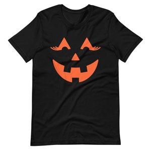 Puede incluir: Camiseta negra con un gr&aacute;fico de cara de calabaza naranja. La calabaza tiene pesta&ntilde;as y una amplia sonrisa.