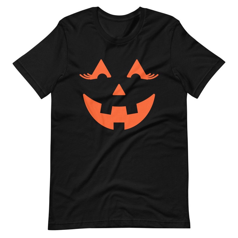 Puede incluir: Camiseta negra con un gr&aacute;fico de cara de calabaza naranja. La calabaza tiene pesta&ntilde;as y una amplia sonrisa.
