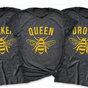 May include: Three gray t-shirts with yellow bee graphics and text. The shirts read "Worker", "Queen", and "Drone".