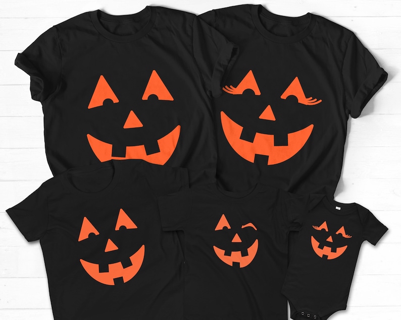 Puede incluir: Conjunto de cinco camisetas negras con caras de calabaza naranja. Las camisetas presentan diferentes expresiones, incluyendo una calabaza gui&ntilde;ando un ojo, una calabaza con pesta&ntilde;as y una cara de calabaza normal.