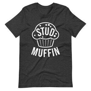 May include: A dark heather grey t-shirt with a white graphic of a cupcake with the word "STUD" inside and the word "MUFFIN" below.