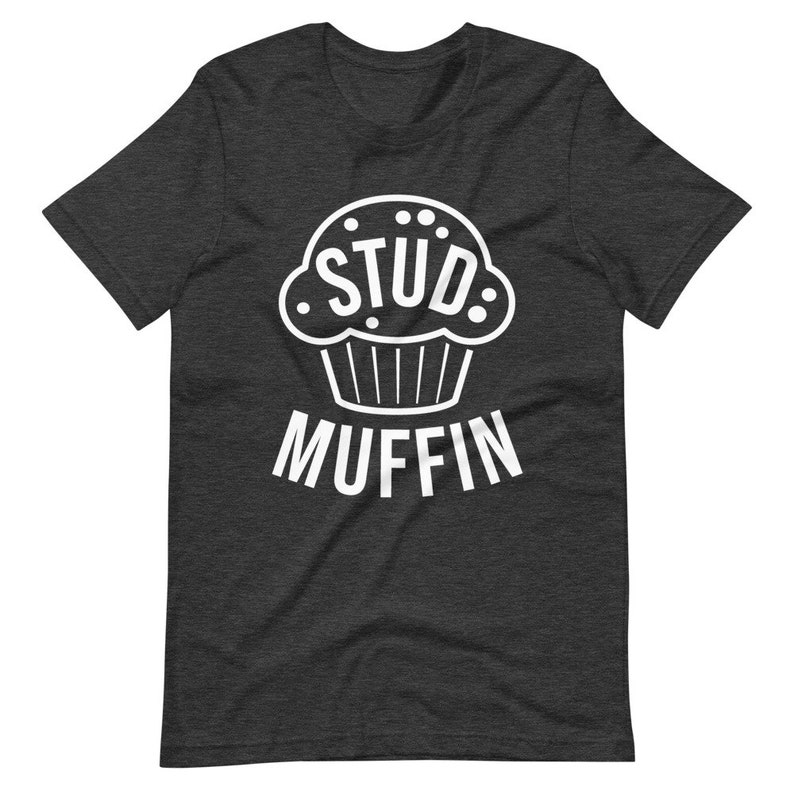 May include: A dark heather grey t-shirt with a white graphic of a cupcake with the word "STUD" inside and the word "MUFFIN" below.