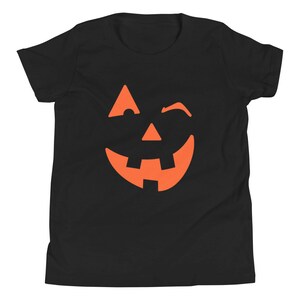 Puede incluir: Camiseta negra para ni&ntilde;os con un gr&aacute;fico de cara de calabaza naranja gui&ntilde;ando un ojo.