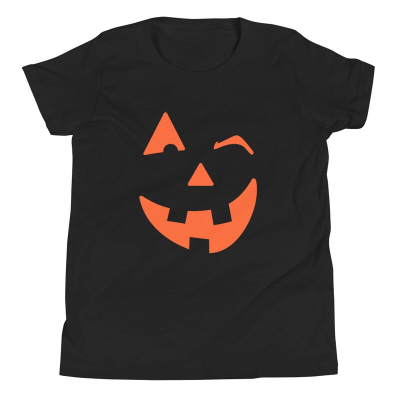 Puede incluir: Camiseta negra para ni&ntilde;os con un gr&aacute;fico de cara de calabaza naranja gui&ntilde;ando un ojo.