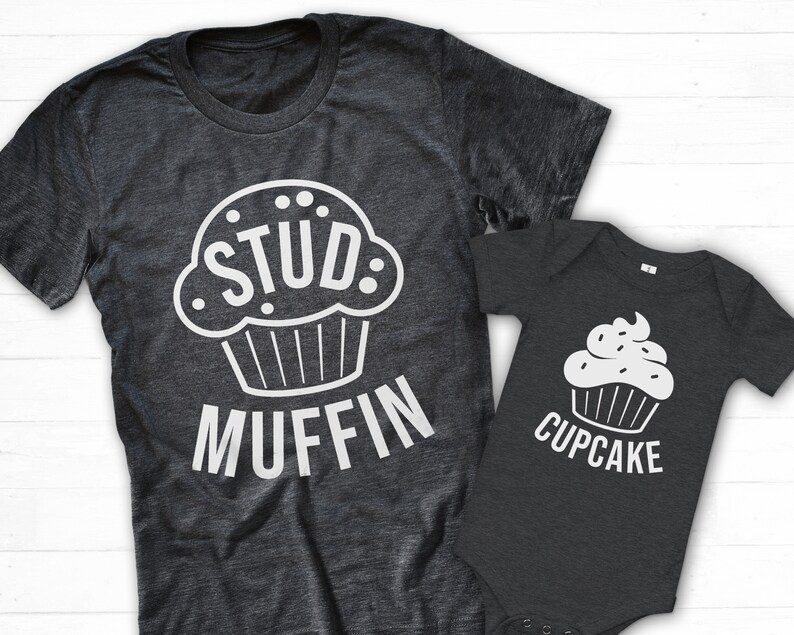 May include: A gray t-shirt with a white cupcake graphic and the text "Stud Muffin". A smaller gray t-shirt with a white cupcake graphic and the text "Cupcake".