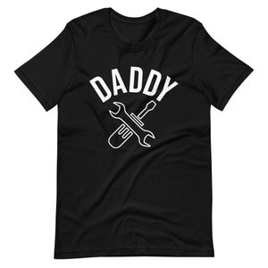 K&ouml;nnte beinhalten: Schwarzes T-Shirt mit wei&szlig;em Text "Daddy" und einem darunter gekreuzten wei&szlig;en Schraubenschl&uuml;ssel und Schraubendreher.