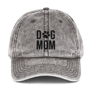 May include: A gray distressed denim baseball cap with black embroidered text that reads "DOG MOM" with a paw print between the words.