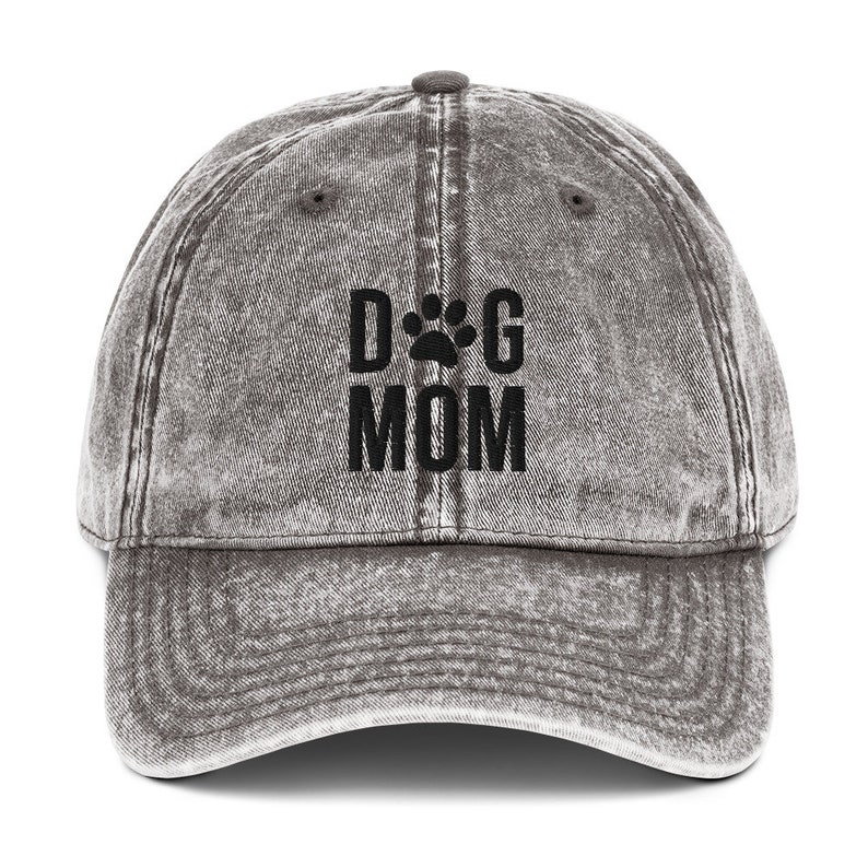 May include: A gray distressed denim baseball cap with black embroidered text that reads "DOG MOM" with a paw print between the words.