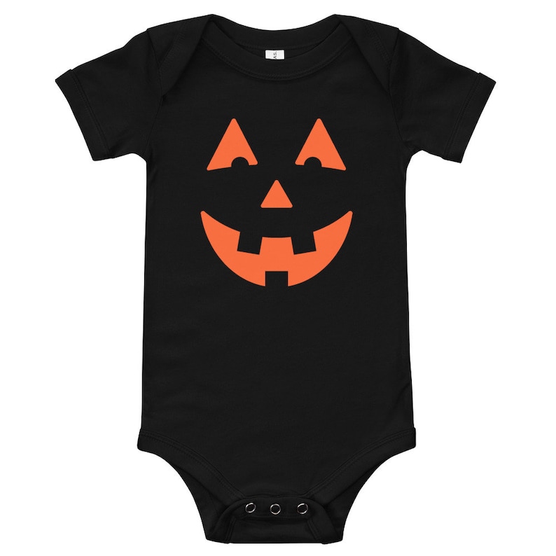 Puede incluir: Mono de beb&eacute; negro con un gr&aacute;fico de cara de calabaza naranja.