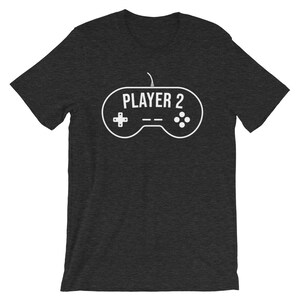 May include: A dark heather grey t-shirt with a white graphic of a video game controller with the text "PLAYER 2" on it.