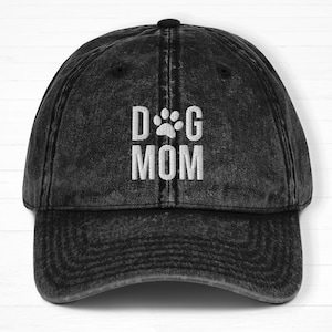 May include: Black distressed denim baseball cap with white embroidered text that reads "DOG MOM" with a paw print between the words.