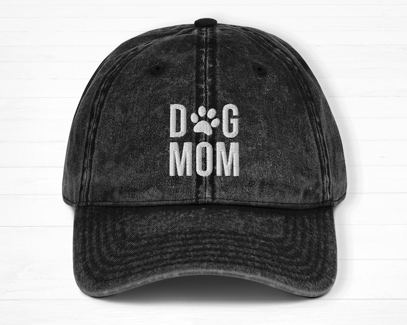 May include: Black distressed denim baseball cap with white embroidered text that reads "DOG MOM" with a paw print between the words.