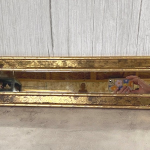 May include: A long, rectangular wall mirror featuring a decorative gold frame with a textured, faux-bamboo finish. The frame displays a distressed, mottled gold leaf pattern throughout its surface, surrounding a clear, horizontal glass mirror pane.