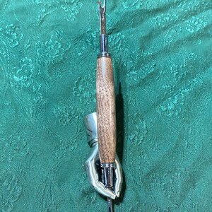 May include: A silver hand-shaped holder with a wooden-handled seam ripper with a silver tip.
