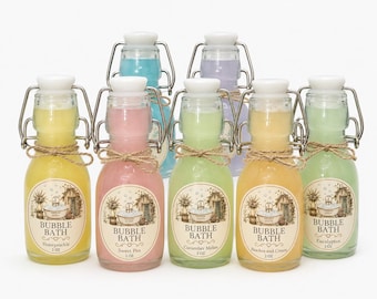 May include: Seven glass bottles with swing-top lids and white stoppers, each filled with colored bubble bath liquid. Labels feature a bathtub illustration and text reading BUBBLE BATH, scent names, and 2 oz. Each bottle has a twine bow.