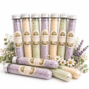 May include: A collection of nine clear glass test tubes filled with colorful bath salts, each sealed with a silver cap and featuring a label that reads BATH SALTS. The tubes contain purple, yellow, and green crystals, arranged in a group.