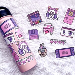 May include: A pink water bottle with various stickers on it. The stickers feature images of a games console, a milk carton, a floppy disk, a computer screen, a cup of boba tea, and a pair of headphones. The stickers also include text such as "Life has no respawns" and "Save your progress".