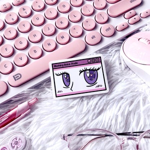 May include: A pink keyboard with round keys, a pink mouse, a pink pen, clear glasses and a sticker with a cartoon illustration of a pair of eyes with stars and hearts. The sticker reads "Blushing Boba Studio".