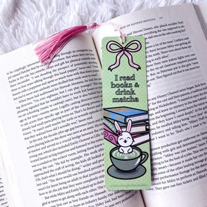May include: A colorful bookmark with the text "I read books & drink matcha" and a cute bunny illustration. The bookmark is placed in an open book with a pink tassel.
