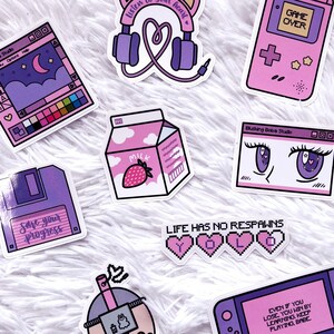 May include: A collection of pink and purple stickers with various designs, including a milk carton with a strawberry, a floppy disk with the text "Save your progress", a games console with the text "Game Over", a window with the text "Blushing Boba Studio" and a pair of eyes, a window with the text "Blushing Boba Studio" and a night sky, a heart with headphones and the text "Listen to your heart", a bubble tea with a straw, a games console with the text "Even if you lose, you win by learning. Keep playing babe", and a pixelated heart with the text "Life has no respawns YOLO".