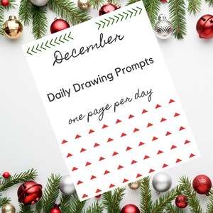 May include: A white sheet with the word "December" and "Daily Drawing Prompts" in black script. The sheet has red triangle accents and the text "one page per day". The image is decorated with Christmas ornaments and greenery.