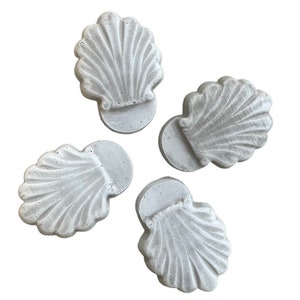 May include: Four white concrete seashells with a textured surface. The seashells are arranged in a circular pattern.