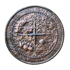 May include: Bronze-colored circular medallion with a compass design. The center features a cross with N, W, E, and S markings. The quadrants depict seasonal imagery: trees, flowers, sun, and harvest. The outer ring has text: "TO EVERY THING THERE IS A SEASON AND A TIME TO EVERY PURPOSE UNDER HEAVEN."