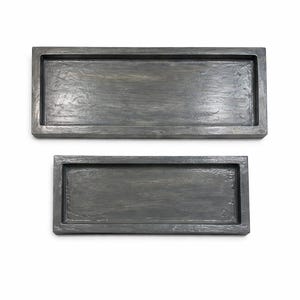 May include: Two rectangular wooden trays with a distressed gray finish. The trays have raised edges and a textured surface, suggesting a rustic or farmhouse style. The trays are likely used for serving or display.