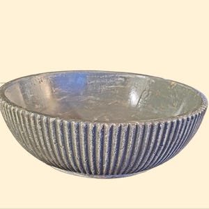 May include: A gray ceramic bowl with a ribbed design. The bowl is round and has a smooth, slightly textured surface.