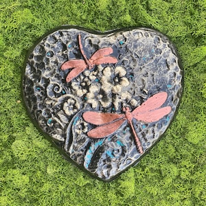 May include: A heart-shaped stone garden stepping stone with a black and white floral design and two copper-colored dragonflies.