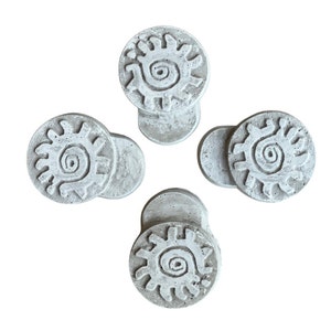 May include: Four white concrete coasters with a raised design of a sun with a spiral in the center.