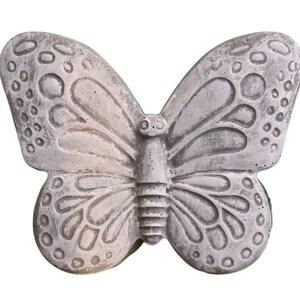 May include: A gray butterfly-shaped decorative object. The butterfly has detailed wing patterns with circular and oval shapes. The object appears to be made of stone or a similar material, with a textured surface and a weathered appearance.