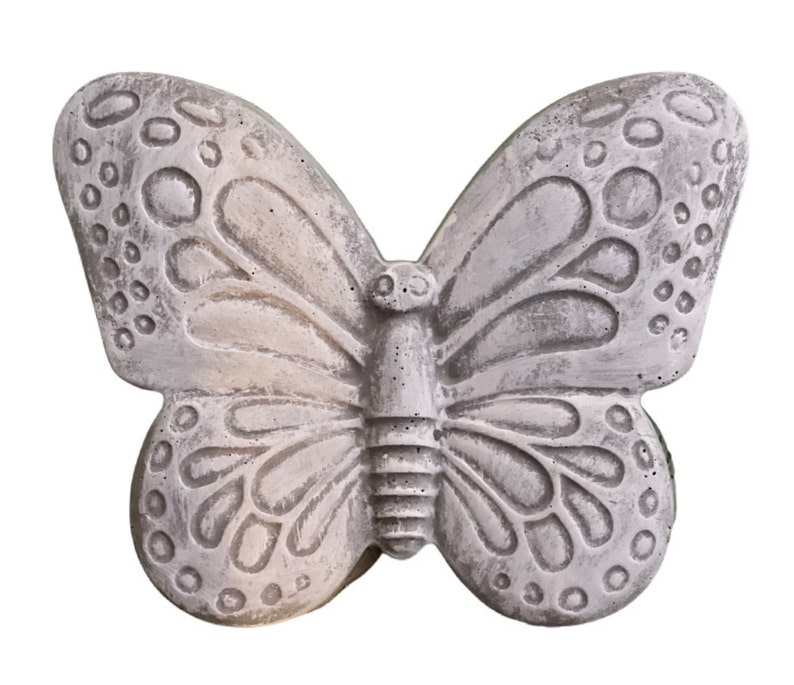 May include: A gray butterfly-shaped decorative object. The butterfly has detailed wing patterns with circular and oval shapes. The object appears to be made of stone or a similar material, with a textured surface and a weathered appearance.