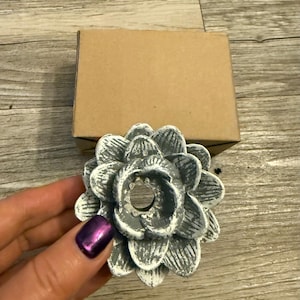 May include: A white and gray ceramic flower-shaped candle holder with a hole in the center. The holder has a distressed finish and a rustic look.