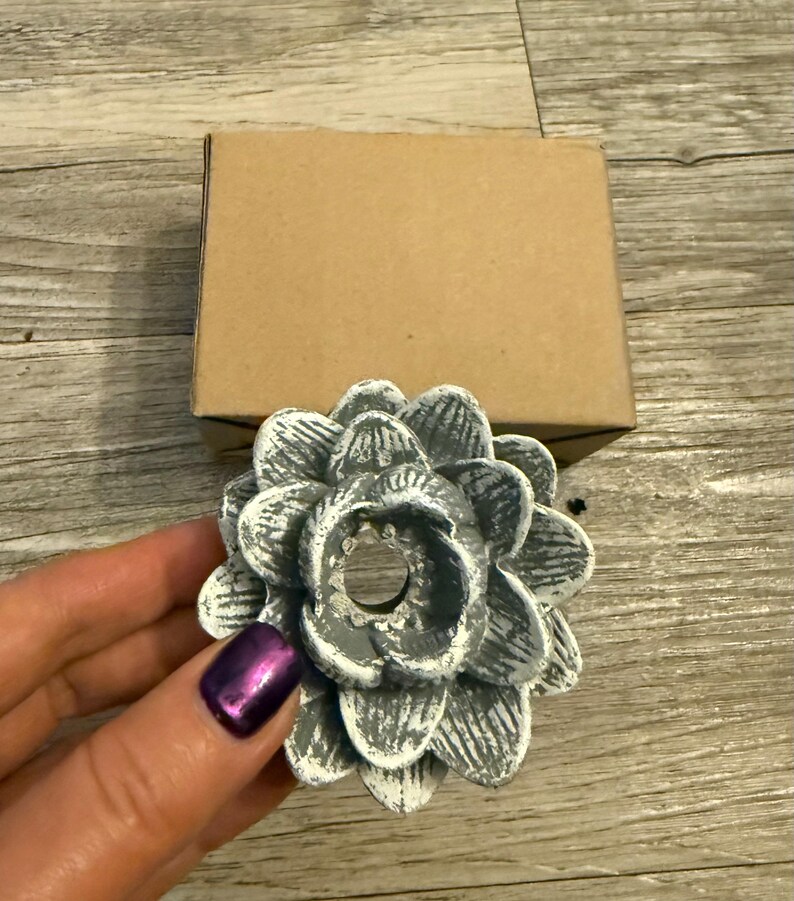 May include: A white and gray ceramic flower-shaped candle holder with a hole in the center. The holder has a distressed finish and a rustic look.