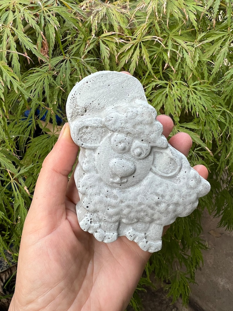 Puede incluir: Una figurita de oveja de hormig&oacute;n gris con una superficie texturizada. La oveja tiene una cabeza redonda con una nariz peque&ntilde;a y ojos grandes. La oveja est&aacute; de pie sobre cuatro patas.