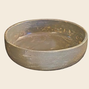 May include: A large, round, gray ceramic bowl with a distressed finish. The bowl has a wide, shallow opening and a slightly rounded bottom.