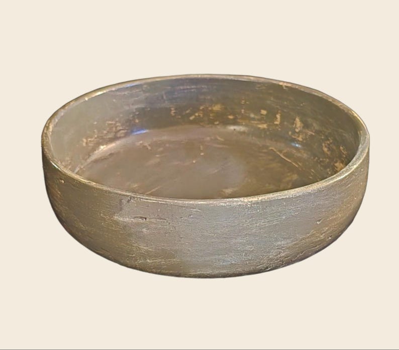 May include: A large, round, gray ceramic bowl with a distressed finish. The bowl has a wide, shallow opening and a slightly rounded bottom.
