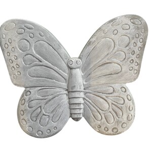 May include: A decorative, gray butterfly sculpture with detailed wing patterns and a textured finish. The butterfly has a symmetrical design with rounded wing tips and a segmented body, perfect for garden decor.