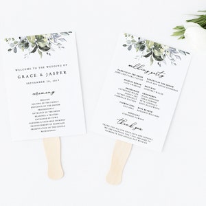 Puede incluir: Dos abanicos de boda blancos con mangos de madera. Cada abanico presenta un texto elegante y un diseño floral en acuarela en verde y gris. Un abanico dice "Bienvenida a la boda de Grace & Jasper" y el otro enumera la fiesta de bodas.