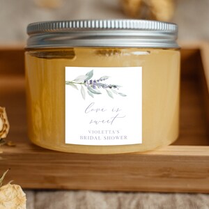 May include: A clear glass jar with a silver lid filled with a yellow substance. The jar has a white label with a watercolor illustration of lavender flowers and leaves. The label reads "Love is sweet" and "Violetta's Bridal Shower".