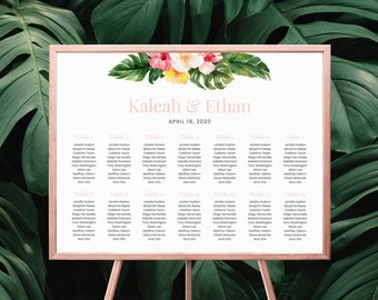 May include: A wedding seating chart with a tropical theme. The chart is printed on white paper and framed in a light wood frame. The top of the chart features a watercolor illustration of tropical leaves and flowers in shades of pink, yellow, and green. The text "Kaleah & Ethan" is printed in pink script font and the date "April 18, 2020" is printed below in black font. The chart lists the names of guests assigned to each table.