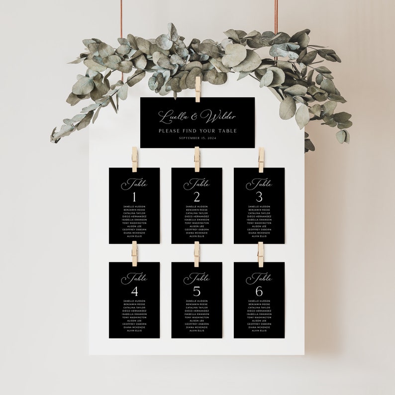 May include: Black and white wedding seating chart with the names "Luella & Wilder" and the date "September 15, 2014". The chart is hung on a white wall with greenery hanging from the top.