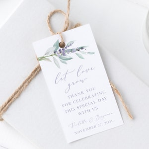 Puede incluir: Una etiqueta de regalo de boda blanca con una ilustración de acuarela de flores de lavanda y hojas verdes. El texto en la etiqueta dice "let love grow" e incluye los nombres de la pareja y la fecha de la boda: Violitla & Buyanes, 27 de noviembre de 2021.