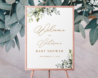 May include: A white welcome sign with gold lettering and green watercolor leaves. The sign reads "Welcome to Victoria's Baby Shower November 21, 2020".